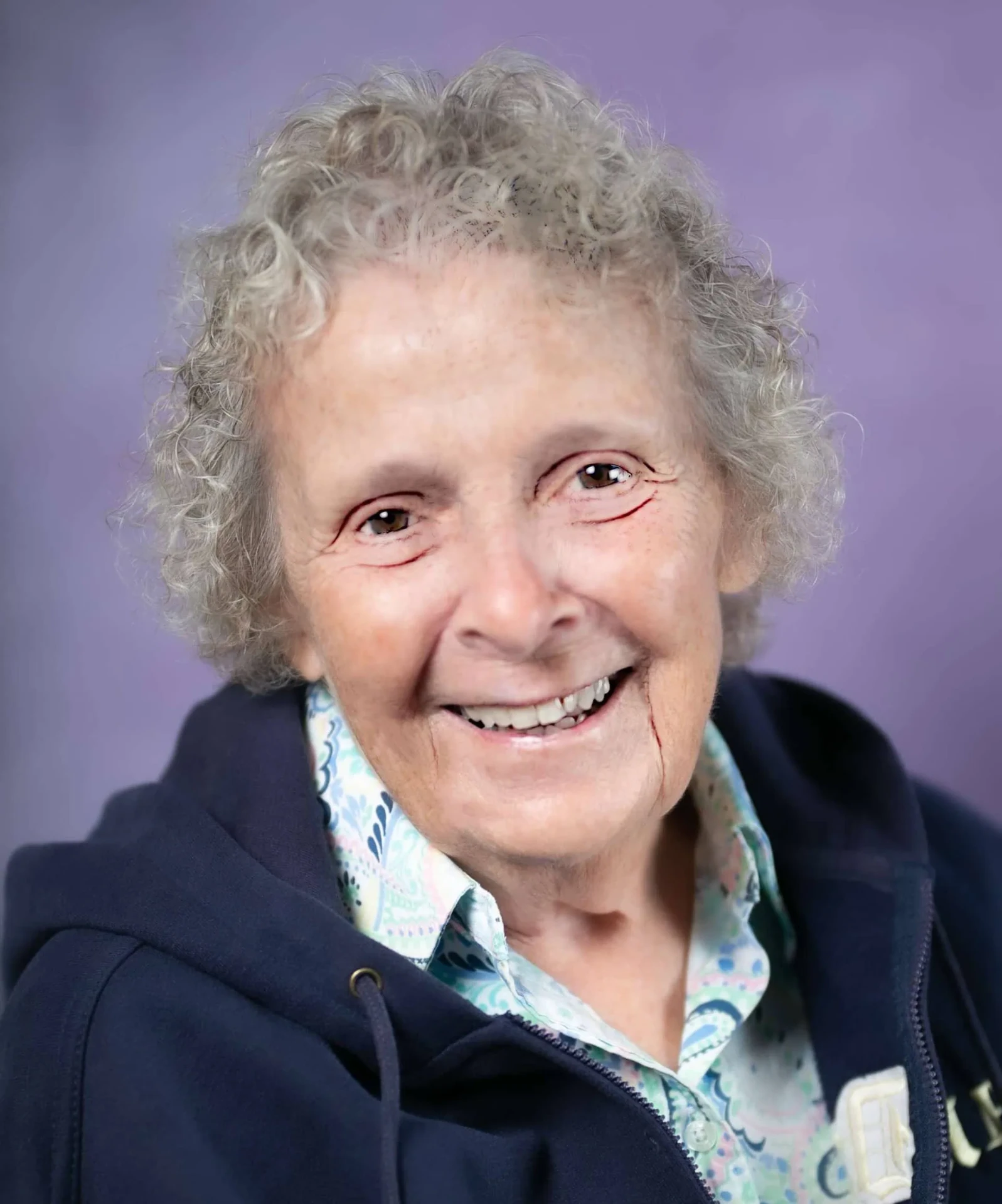 Sister Sarah Mulligan smiling in a portrait, wearing a navy zip hoodie over a pastel patterned blouse